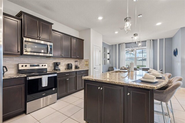 kitchen with sink, pendant lighting, decorative backsplash, a center island with sink, and appliances with stainless steel finishes