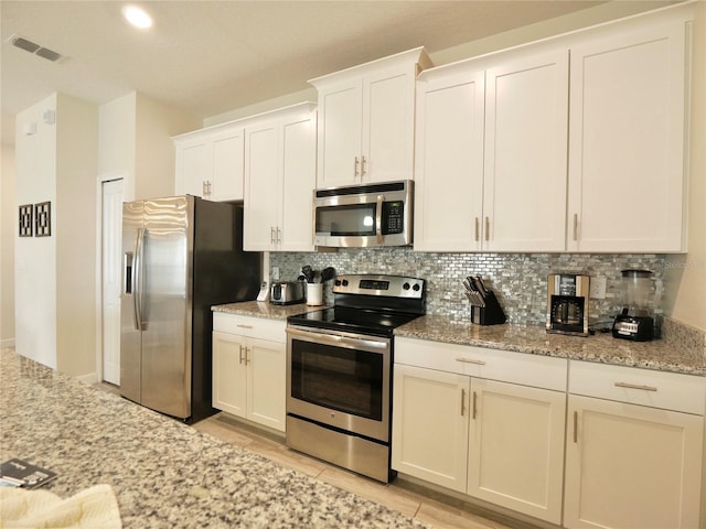 kitchen featuring backsplash, light stone counters, white cabinetry, and stainless steel appliances