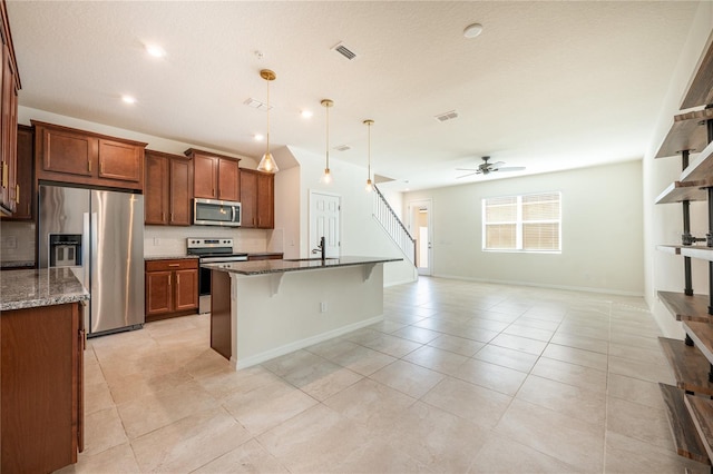 kitchen with dark stone counters, ceiling fan, pendant lighting, and appliances with stainless steel finishes