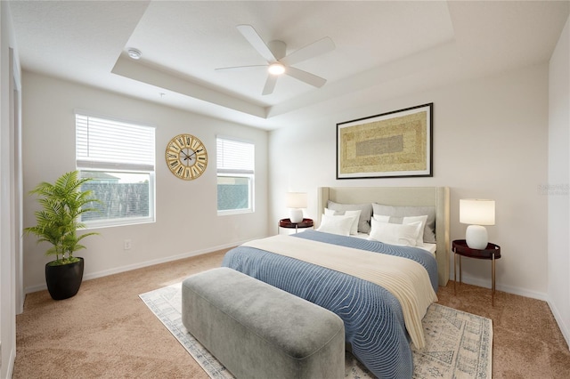 carpeted bedroom with a raised ceiling and ceiling fan