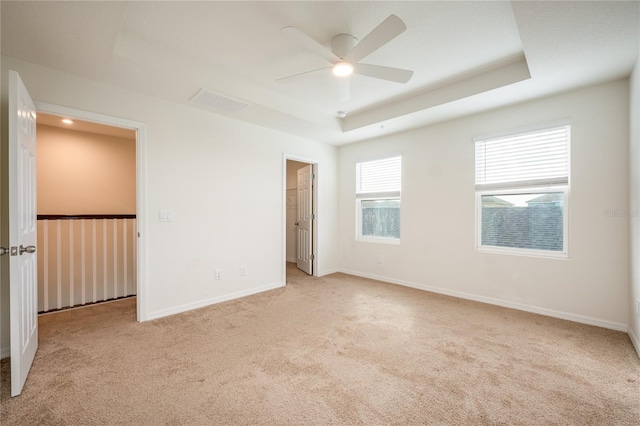 unfurnished bedroom with a raised ceiling, ceiling fan, a closet, and light colored carpet