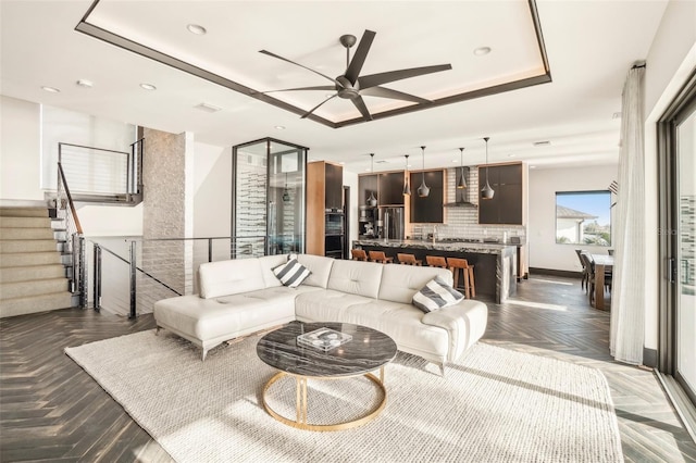 living room featuring a raised ceiling, ceiling fan, and dark parquet flooring