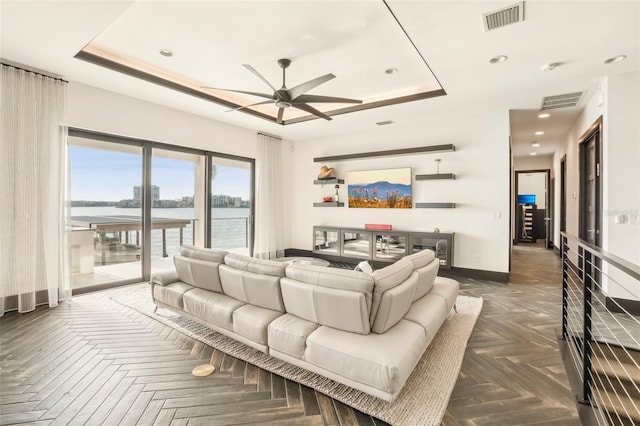 living room featuring a raised ceiling, ceiling fan, dark parquet floors, and a water view