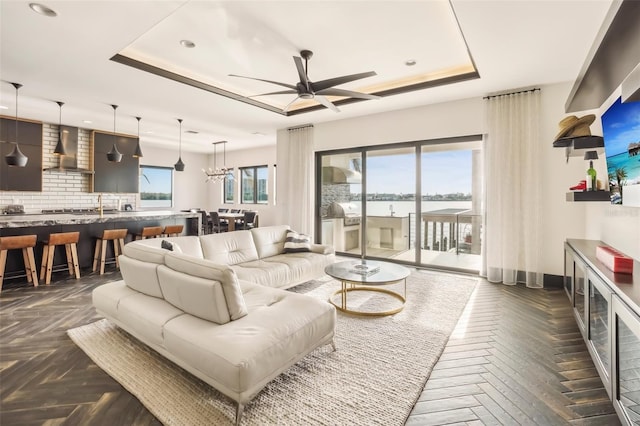 living room featuring dark parquet floors, a raised ceiling, and ceiling fan with notable chandelier