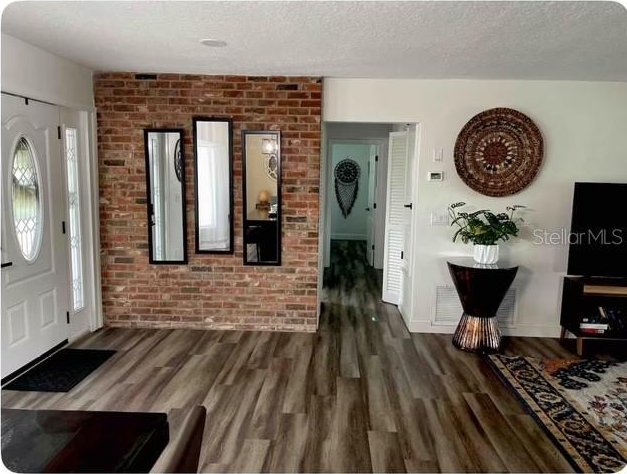 foyer with dark hardwood / wood-style floors, a textured ceiling, and brick wall