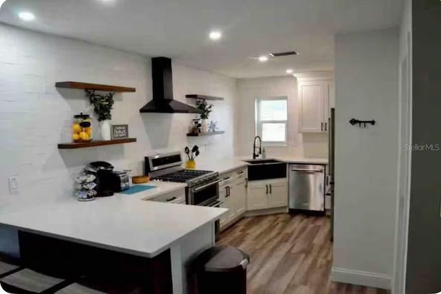 kitchen featuring white cabinets, wall chimney exhaust hood, kitchen peninsula, and stainless steel appliances