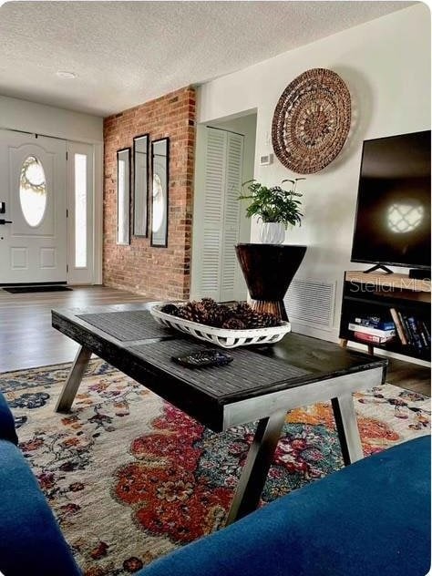 foyer with wood-type flooring, a textured ceiling, and brick wall