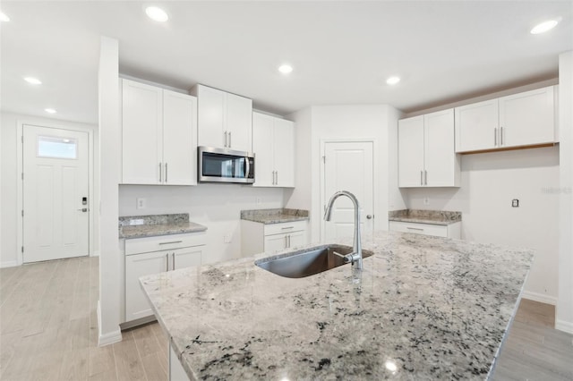 kitchen featuring white cabinetry, light stone countertops, a kitchen island with sink, and sink