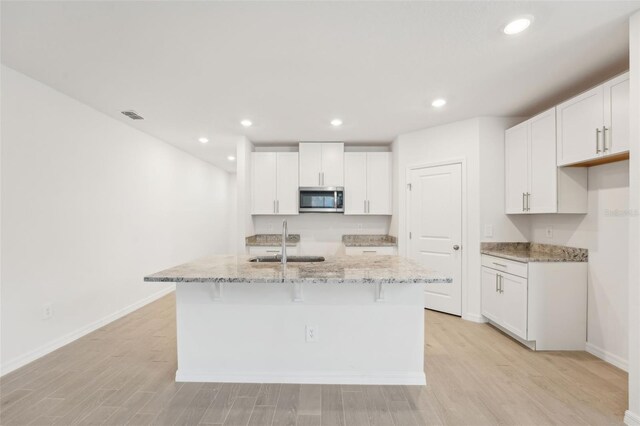 kitchen featuring an island with sink, sink, and white cabinets