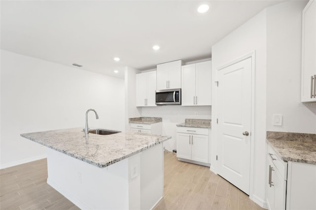 kitchen with sink, light stone countertops, a kitchen island with sink, and white cabinets