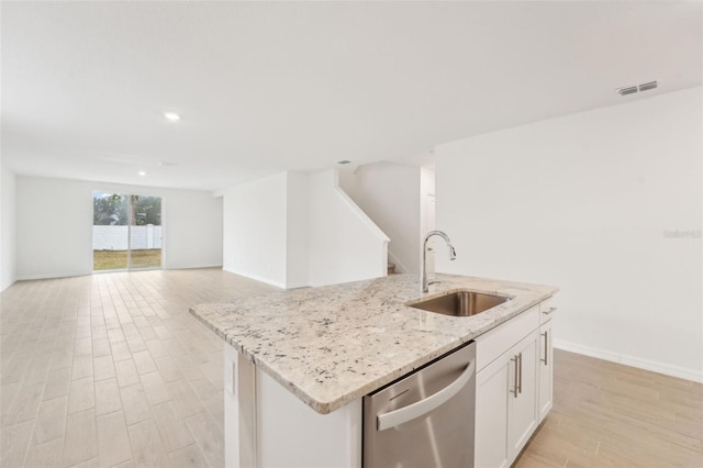 kitchen featuring sink, dishwasher, white cabinetry, light stone counters, and an island with sink