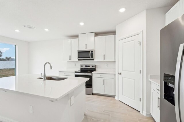 kitchen with sink, stainless steel appliances, white cabinets, and a center island with sink