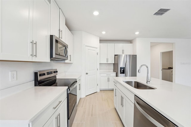 kitchen featuring independent washer and dryer, appliances with stainless steel finishes, sink, and white cabinets