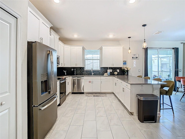 kitchen featuring hanging light fixtures, white cabinets, kitchen peninsula, and appliances with stainless steel finishes