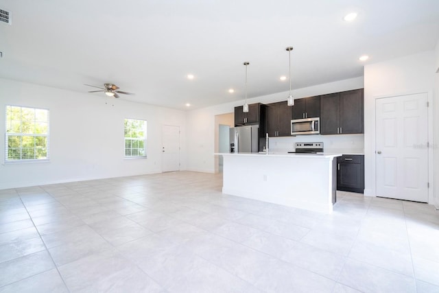 kitchen with pendant lighting, ceiling fan, an island with sink, appliances with stainless steel finishes, and dark brown cabinetry