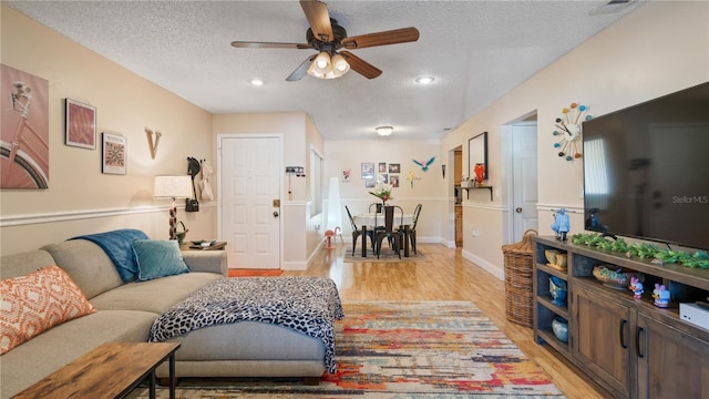 living room with ceiling fan, a textured ceiling, and light wood-type flooring