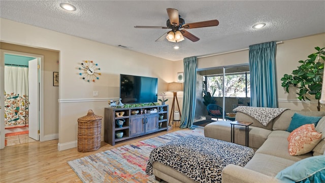 living room with ceiling fan, light hardwood / wood-style floors, and a textured ceiling