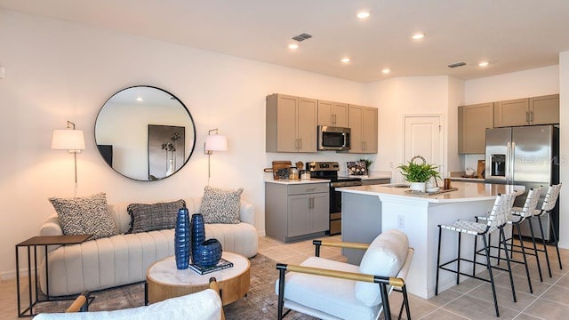 kitchen with gray cabinetry, a breakfast bar, a kitchen island with sink, light tile patterned floors, and stainless steel appliances