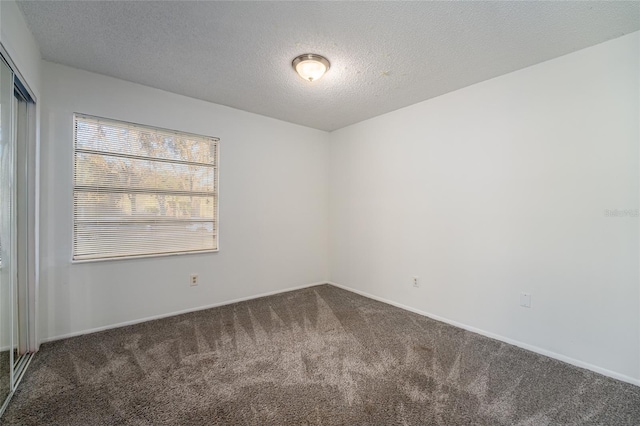 unfurnished room with dark colored carpet and a textured ceiling