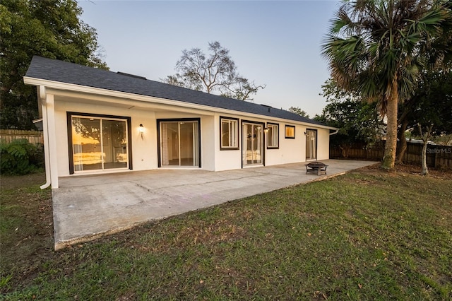 back house at dusk featuring a patio, a fire pit, and a lawn