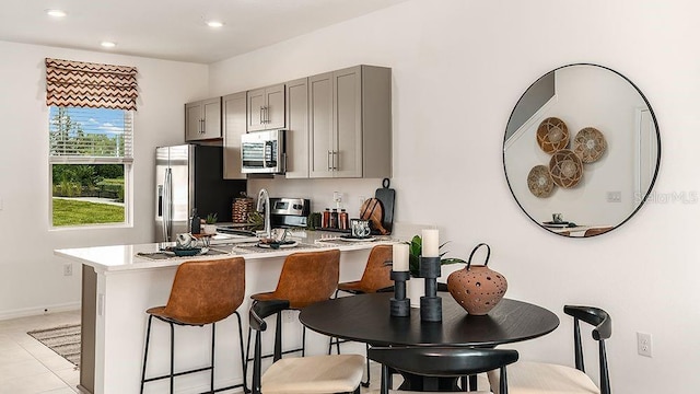 kitchen featuring gray cabinetry, a breakfast bar, light tile patterned floors, and appliances with stainless steel finishes