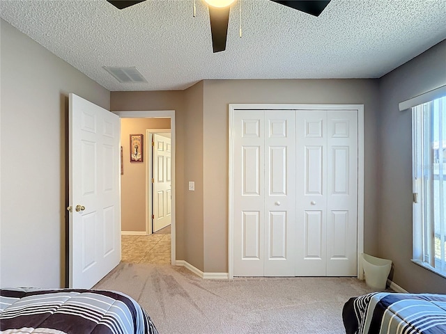 carpeted bedroom with ceiling fan, a closet, and a textured ceiling