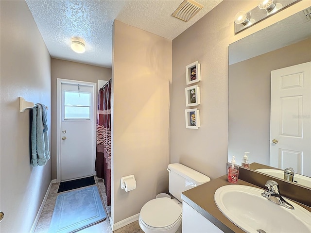 bathroom with tile patterned flooring, vanity, toilet, and a textured ceiling