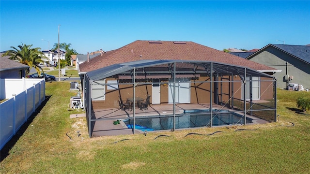 rear view of house with a lawn, glass enclosure, a patio, and a fenced in pool