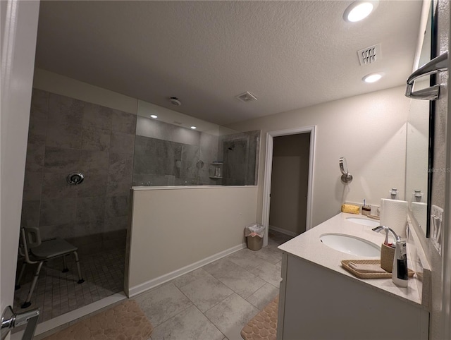 bathroom featuring tile patterned floors, vanity, tiled shower, and a textured ceiling