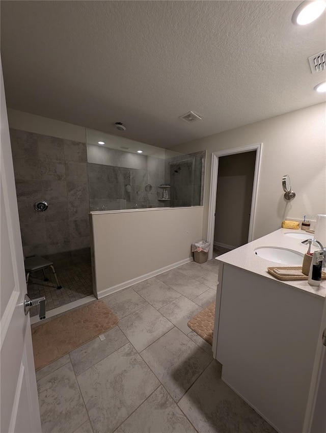 bathroom with a tile shower, vanity, and a textured ceiling