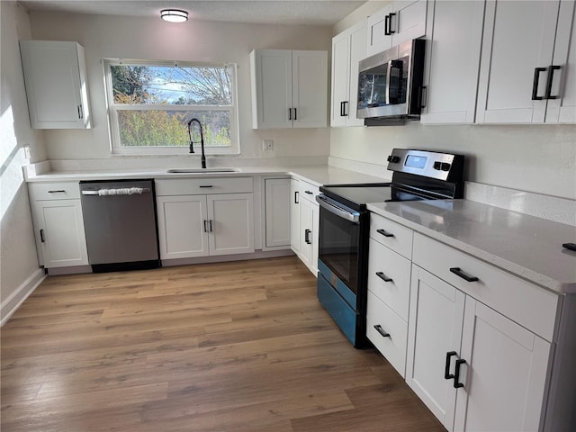 kitchen with sink, white cabinets, light hardwood / wood-style floors, and appliances with stainless steel finishes