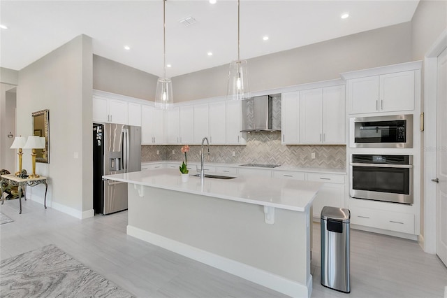 kitchen featuring appliances with stainless steel finishes, sink, wall chimney range hood, white cabinetry, and an island with sink