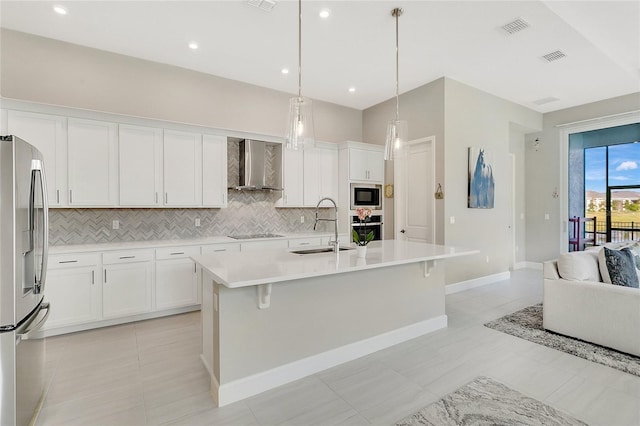 kitchen featuring sink, wall chimney range hood, decorative light fixtures, a center island with sink, and appliances with stainless steel finishes