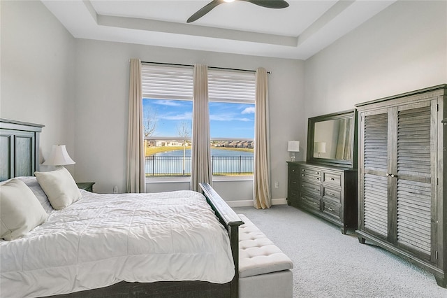 bedroom with a tray ceiling, ceiling fan, a water view, and light carpet