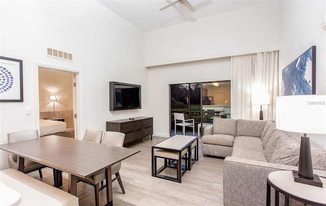 living room with ceiling fan, a high ceiling, and light hardwood / wood-style flooring