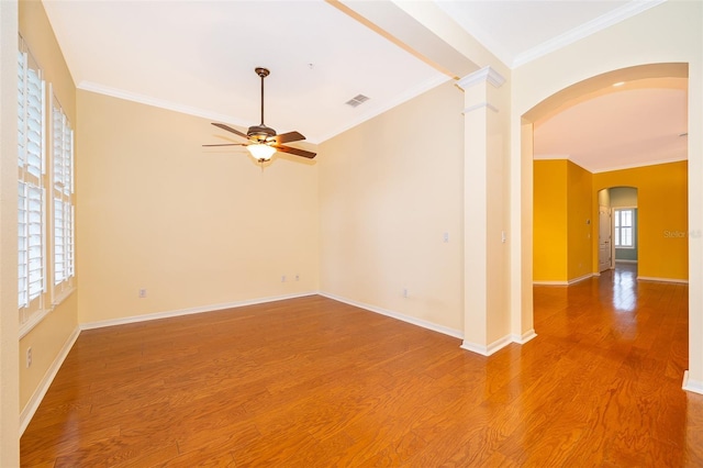 empty room with crown molding, light wood-style floors, arched walkways, a ceiling fan, and visible vents