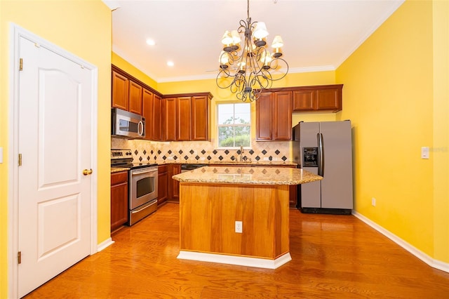 kitchen with an inviting chandelier, a center island, backsplash, light stone countertops, and stainless steel appliances