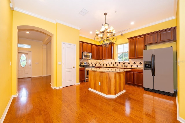 kitchen featuring arched walkways, light wood-type flooring, stainless steel appliances, a notable chandelier, and backsplash