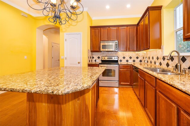 kitchen with a notable chandelier, light wood-style flooring, stainless steel appliances, arched walkways, and a sink