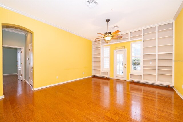 spare room with crown molding, arched walkways, a ceiling fan, baseboards, and built in shelves
