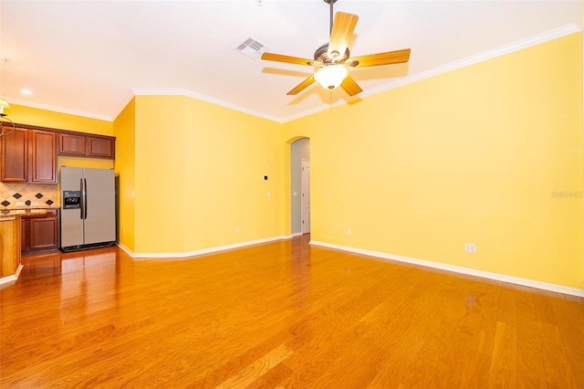 unfurnished living room featuring arched walkways, ornamental molding, visible vents, and light wood-style floors