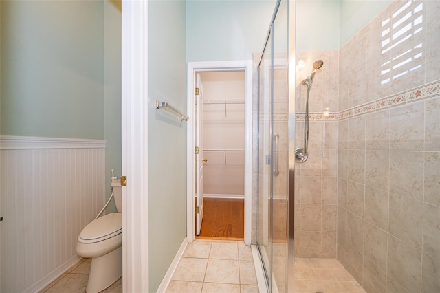 bathroom featuring toilet, a stall shower, a walk in closet, and tile patterned floors