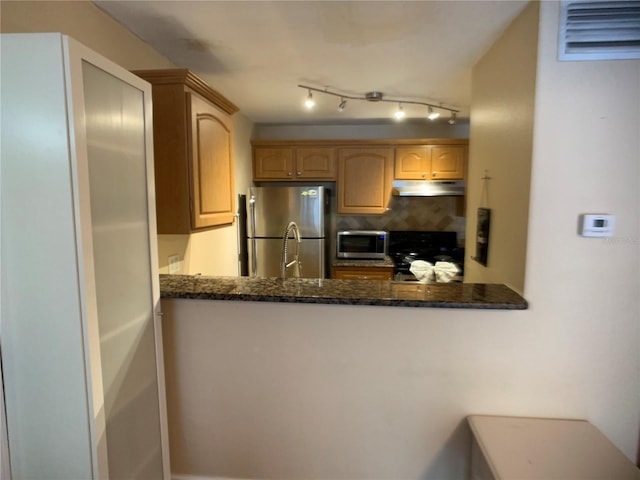 kitchen featuring light brown cabinets, backsplash, stainless steel appliances, and dark stone counters