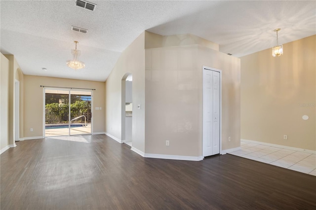 spare room featuring a textured ceiling, hardwood / wood-style flooring, and a notable chandelier