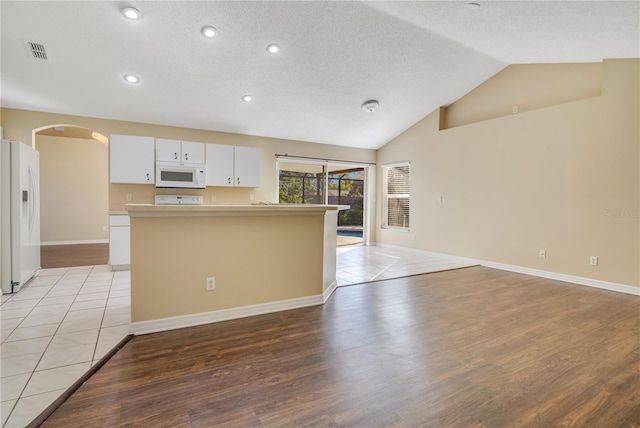 kitchen featuring white cabinetry, lofted ceiling, a textured ceiling, white appliances, and light wood-type flooring