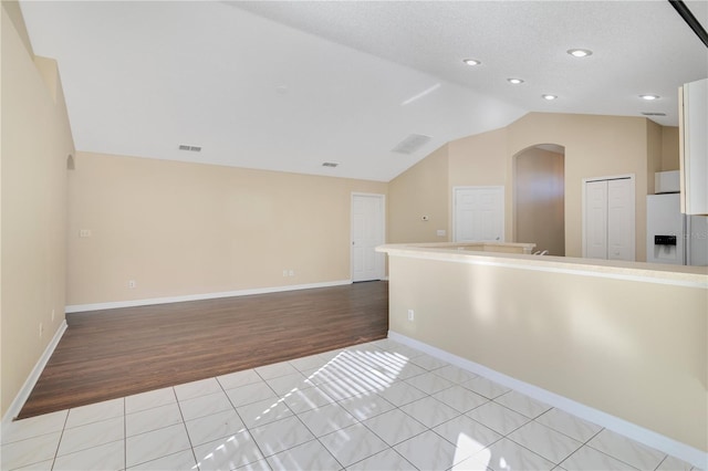 tiled empty room featuring a textured ceiling and vaulted ceiling