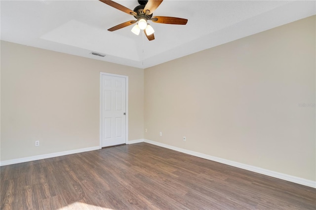 empty room featuring ceiling fan, dark wood-type flooring, and a tray ceiling