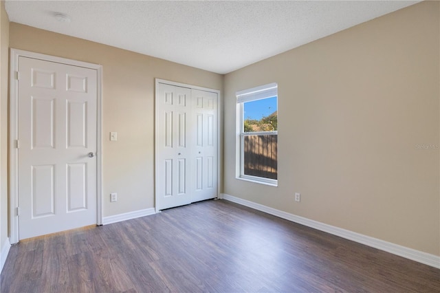 unfurnished bedroom featuring a textured ceiling, dark hardwood / wood-style flooring, and a closet