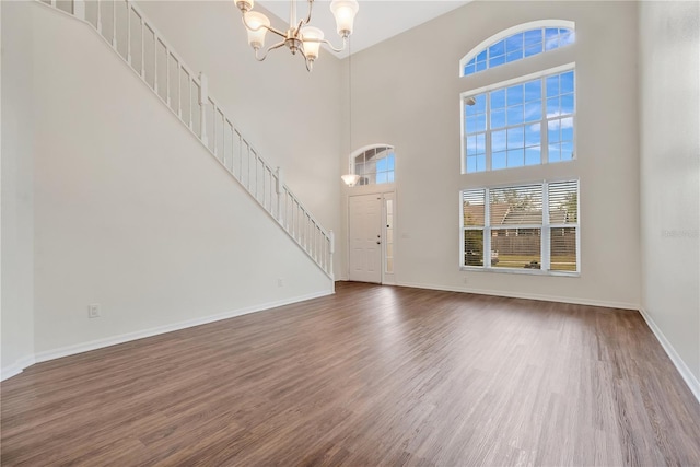 unfurnished living room with dark wood-type flooring, a high ceiling, and an inviting chandelier