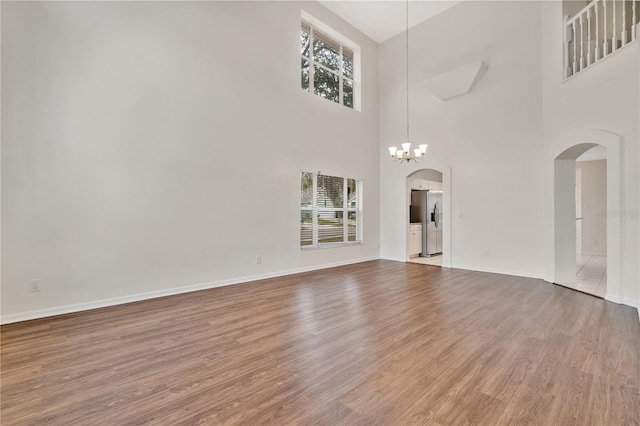 unfurnished living room with a high ceiling, an inviting chandelier, and hardwood / wood-style floors